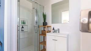 Un baño moderno con ducha de vidrio, muebles blancos y un espejo sobre el lavamanos.