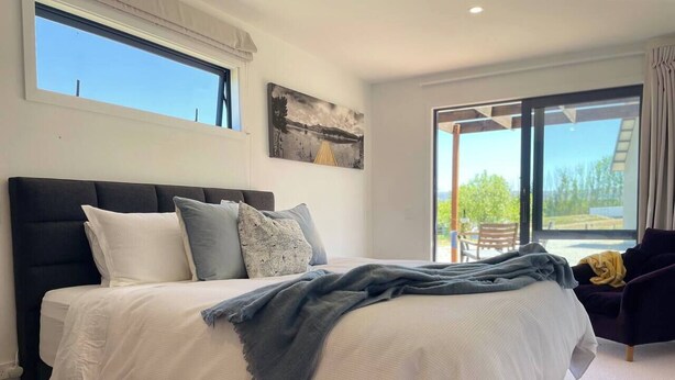 Un dormitorio con una cama grande, un cabecero oscuro y vistas al exterior a través de un ventanal corredera.