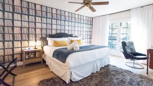 Un dormitorio con una cama grande, una mesita de noche, una silla, un ventilador de techo y una estantería.