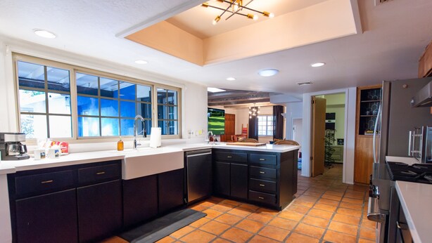 Una cocina moderna con armarios oscuros, un ventanal grande y piso de baldosas.