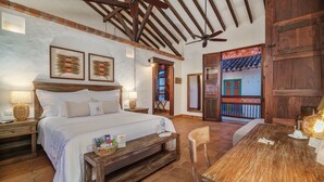 A bedroom with a large bed, wooden headboard, and a ceiling fan. There is a wooden table and a chair in the room. - Casa Linaje Hotel Boutique - Cauca Viejo - Mayores de 10 años (Jericó)