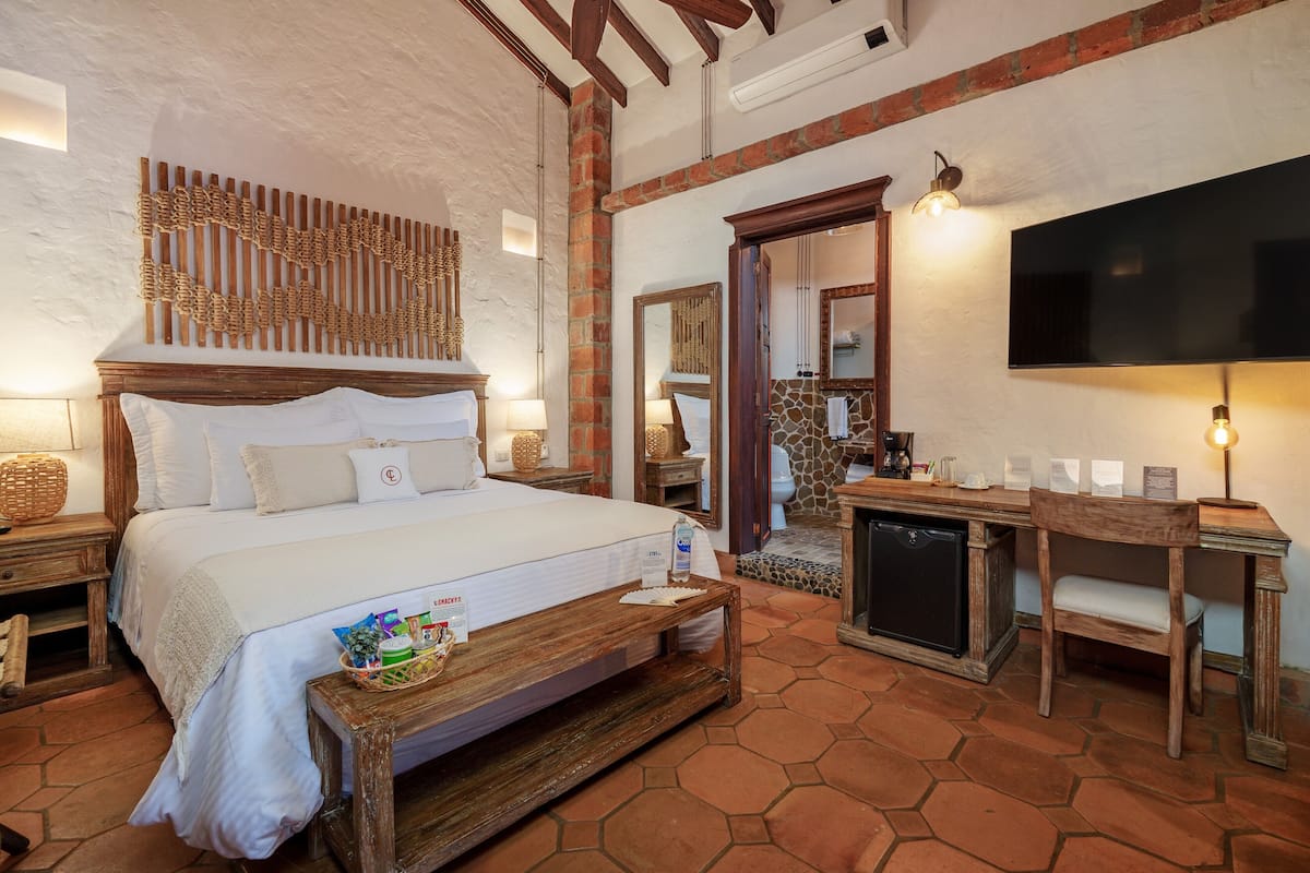 Ein Schlafzimmer mit einem großen Bett, einem Holzkopfstück, Nachttischen, einem Fernseher und einem Schreibtisch mit Stuhl.