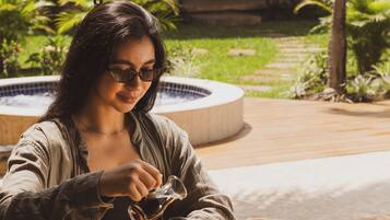 A person sitting at an outdoor table with a meal, a teapot, and a glass of juice.