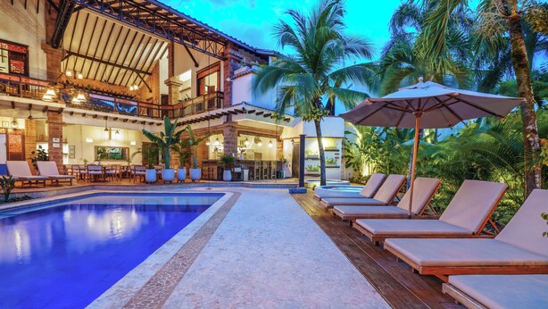 A pool area with lounge chairs and umbrellas, a bar, and a large building with multiple floors and balconies. - Casa Linaje Hotel Boutique - Cauca Viejo - Mayores de 10 años (Jericó)