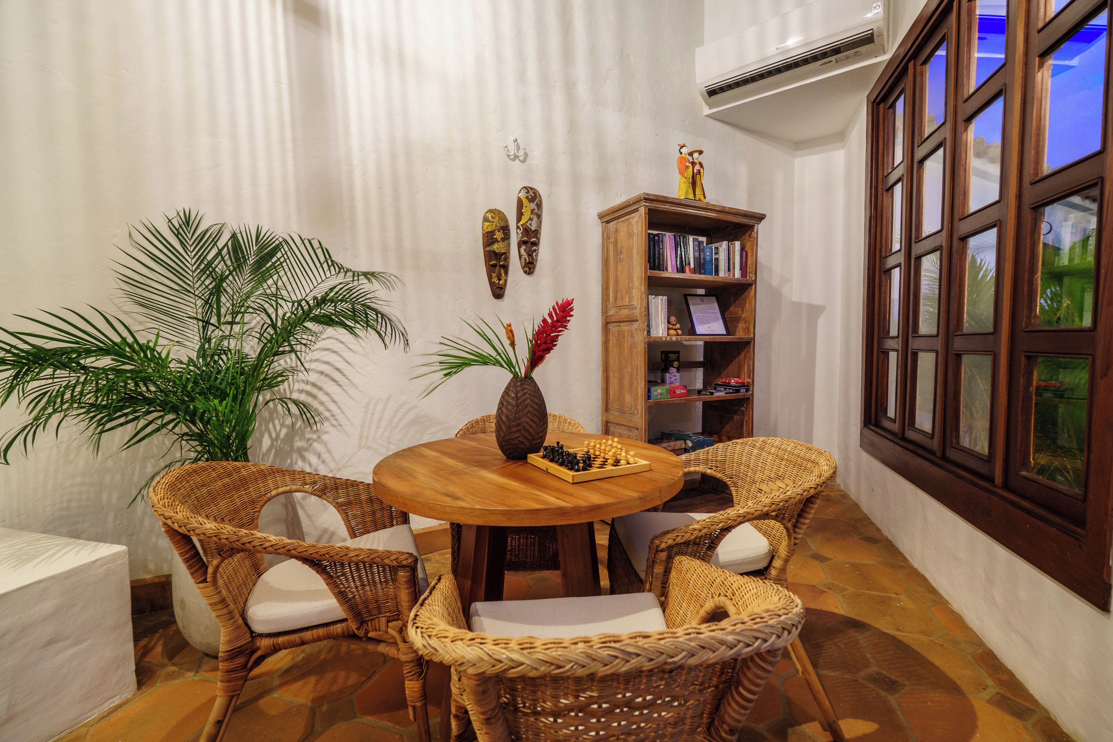 A cozy dining area with a round wooden table, wicker chairs, and a chessboard centerpiece.