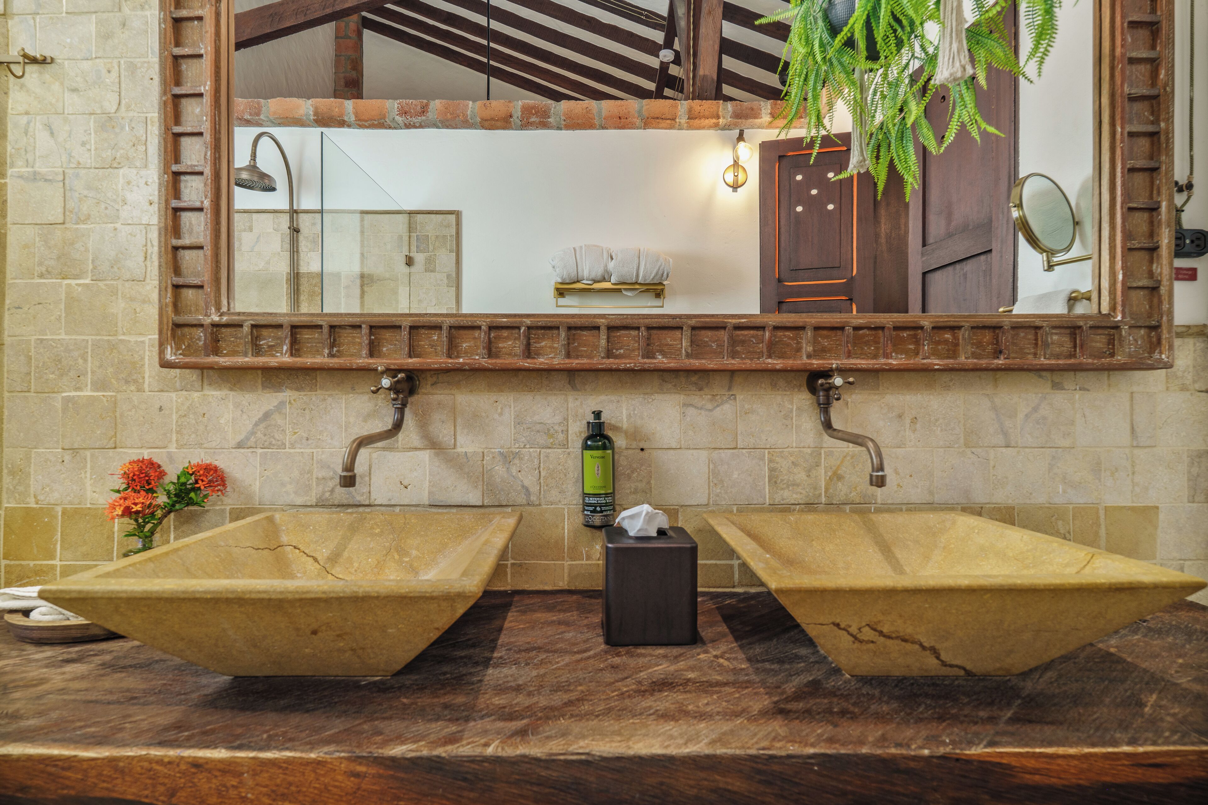 A bathroom with two large, beige stone sinks, a mirror, and a wooden door.