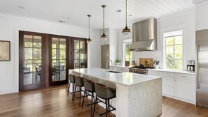 A spacious kitchen with a large island, bar stools, stainless steel appliances, and a view through the sliding glass doors. - Tucked among the treetops and steps to walking trail (Bluffton)