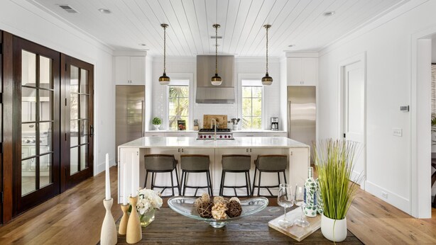 A modern kitchen with white cabinetry, a central island with bar stools, pendant lighting, and a dining table set with candles and decorative items. - Tucked among the treetops and steps to walking trail (Bluffton)