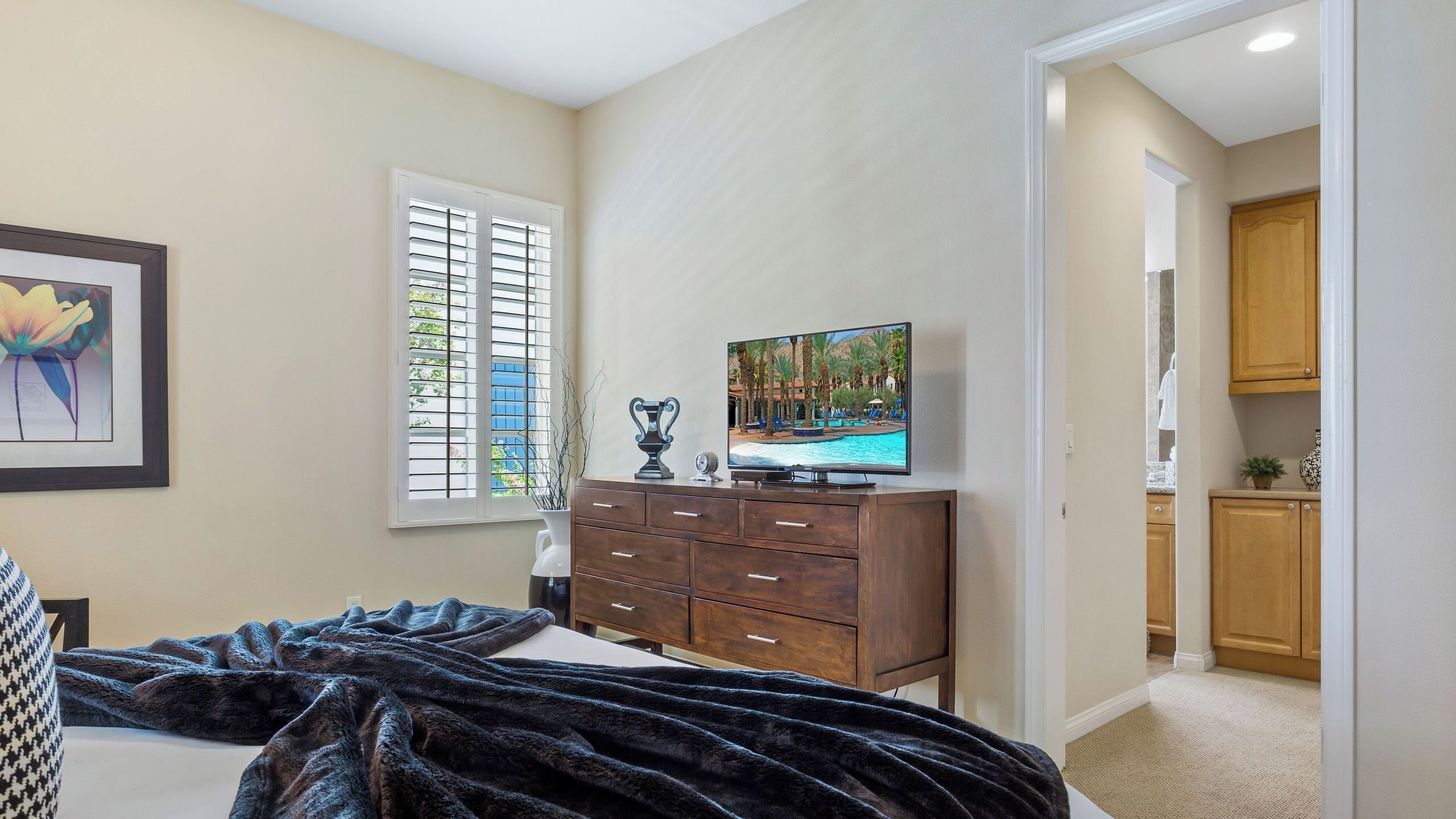 Een slaapkamer met een bed, een dressoir, een televisie en een raam met zonwering.