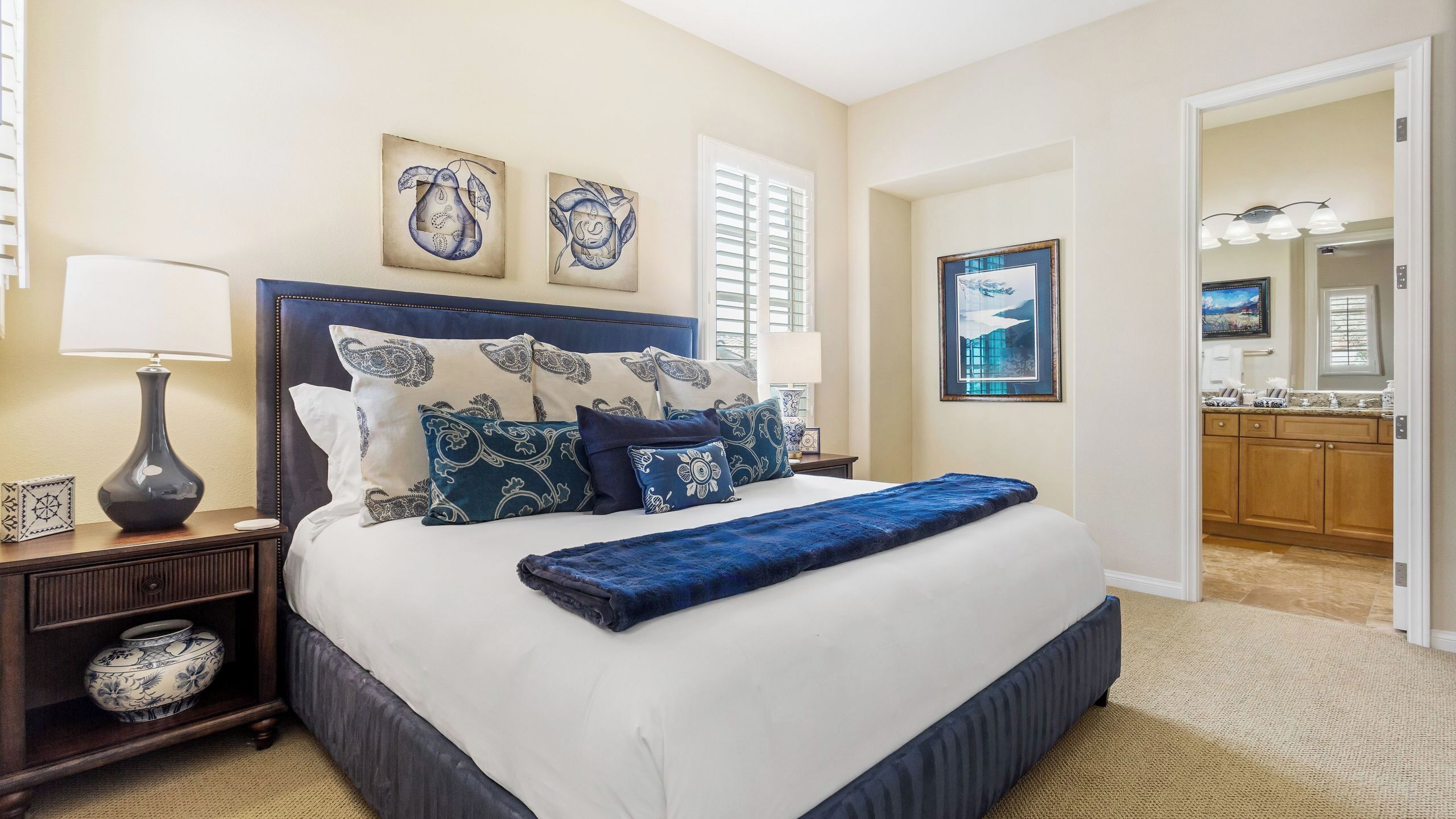 A bedroom with a large bed, bedside tables, a lamp, and artwork on the walls.