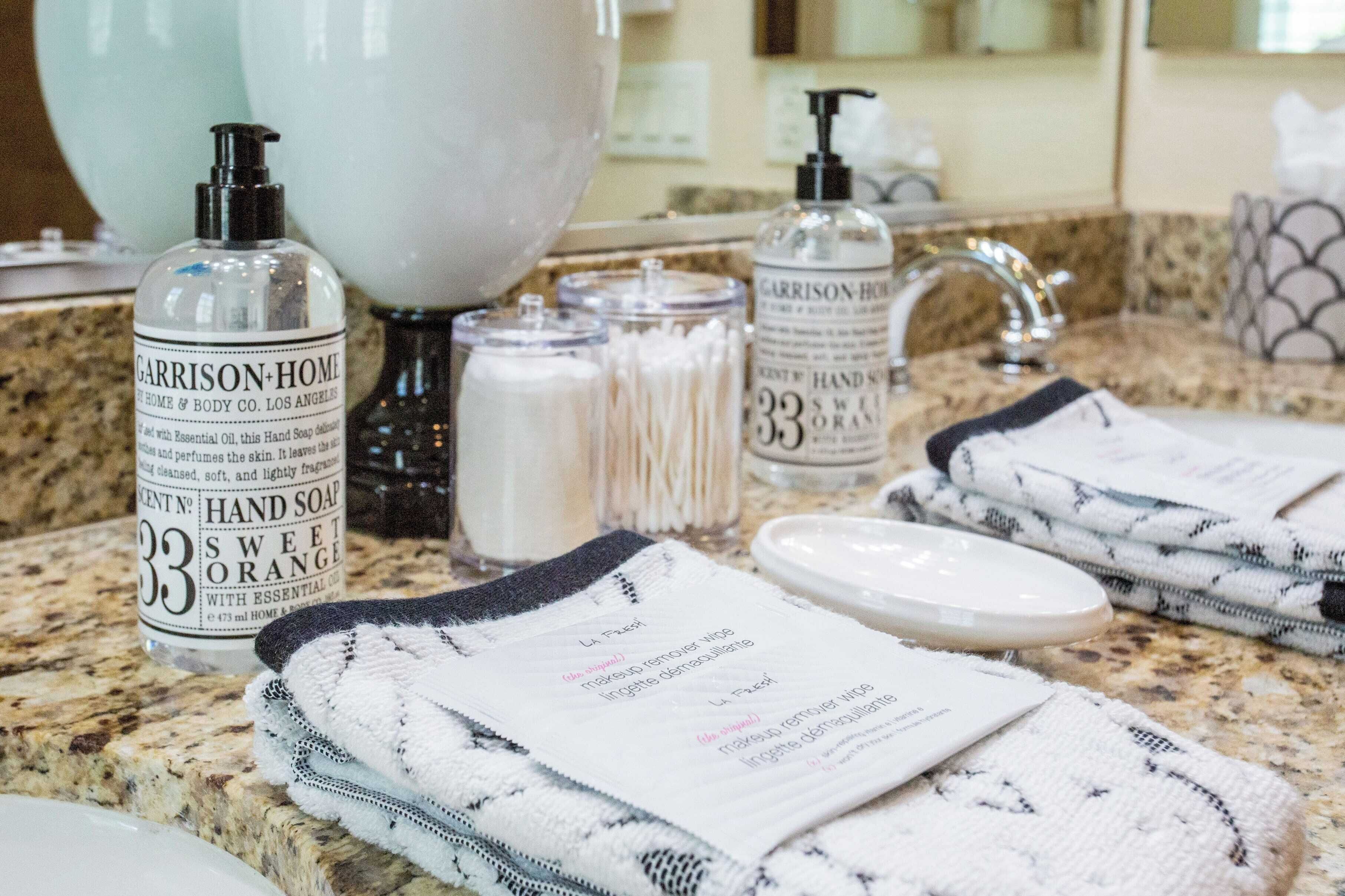A bathroom counter with toiletries, including a bottle of hand soap, a soap dispenser, and a towel with instructions.
