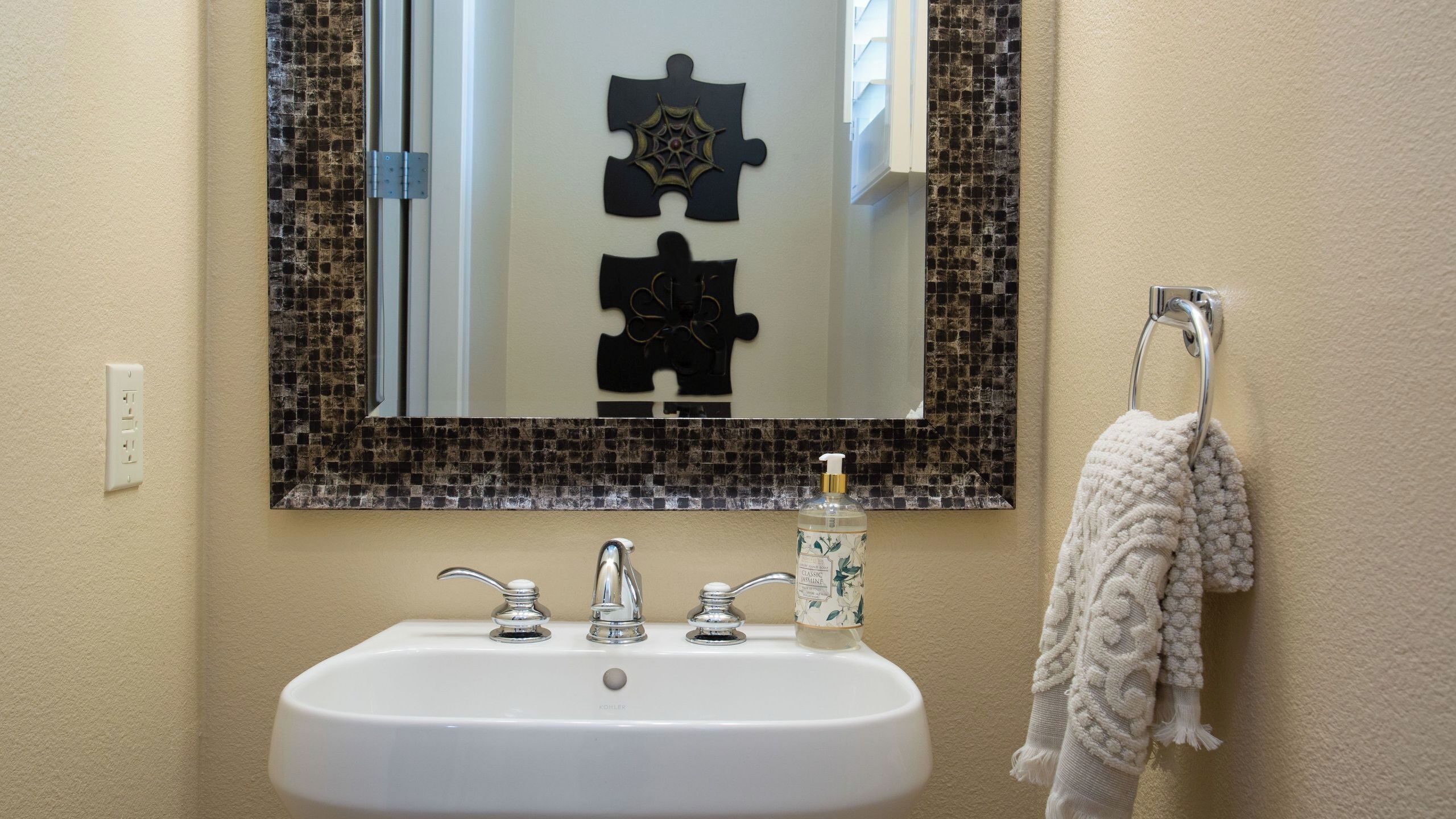 A bathroom with a white sink, two faucets, a mirror with a puzzle piece design, and a towel rack with a towel.