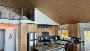 Cocina moderna con gabinetes de madera, refrigerador de acero inoxidable, una isla de mármol con taburetes y un balcón con vistas.