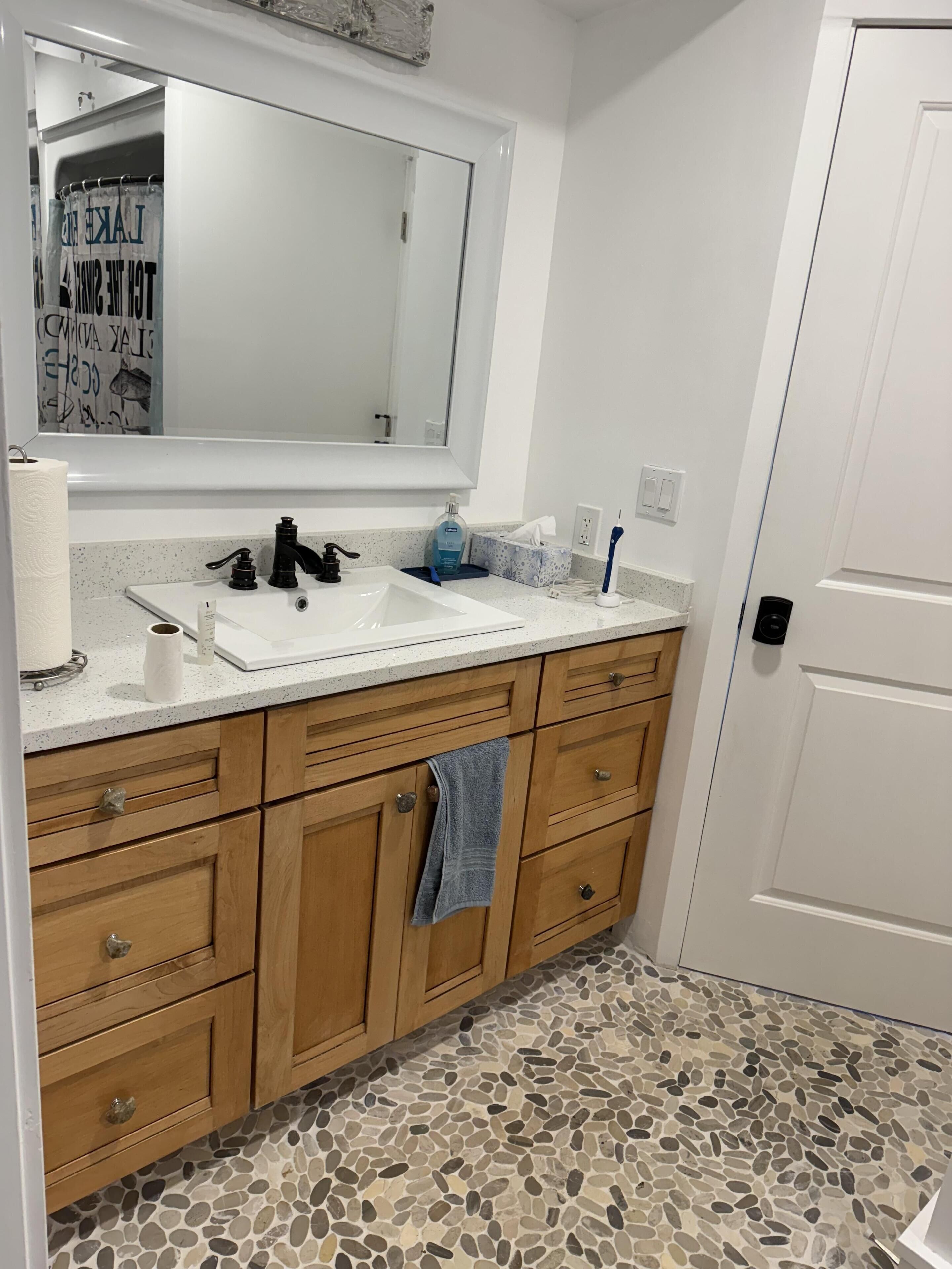 Une salle de bain avec un lavabo blanc, des meubles en bois, un miroir et un sol carrelé.