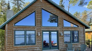 Una cabaña de troncos con ventanas grandes y un área de terraza con sillas.