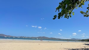 Una spiaggia con cielo sereno, montagne in lontananza e alcune persone che passeggiano.