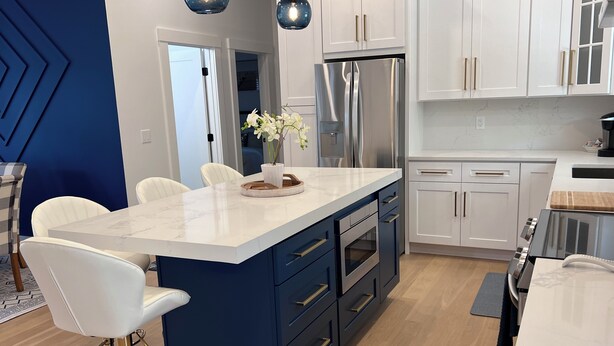 Una cocina moderna con armarios blancos, una isla central con cajones azules y electrodomésticos de acero inoxidable.
