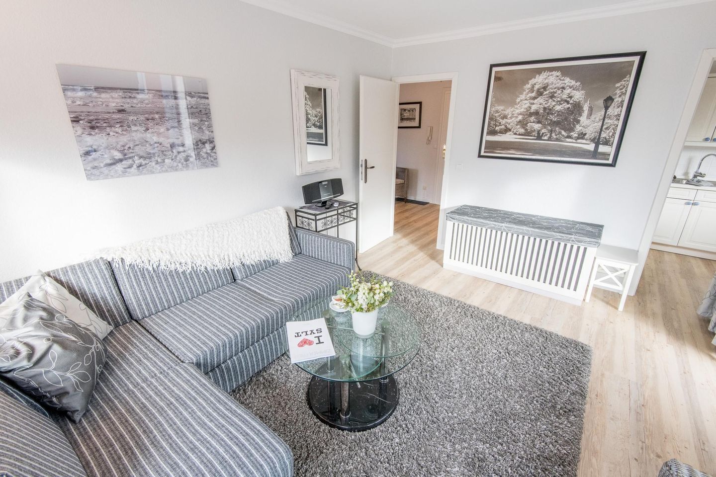 A modern living room with a striped sofa, a glass coffee table with flowers, and a framed picture on the wall.