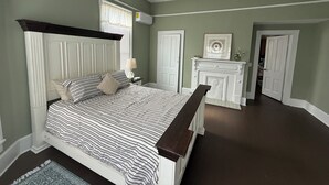Un dormitorio con cama, ventilador de techo, chimenea y puerta que da a otra habitación.