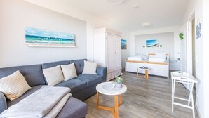 Ein modernes Wohnzimmer mit einem grauen Sofa, einem kleinen runden Tisch und einem Bett im Hintergrund.