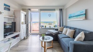 Ein modernes Wohnzimmer mit grauem Sofa, Fernseher und Balkon mit Meerblick.