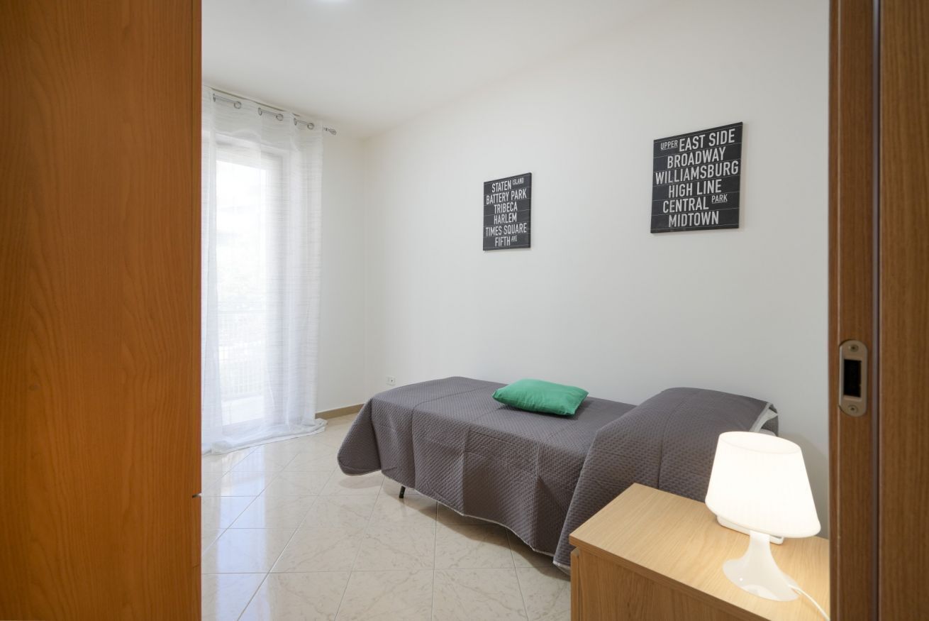 A room with a bed, a bedside table with a lamp, and two signs on the wall listing nearby locations.
