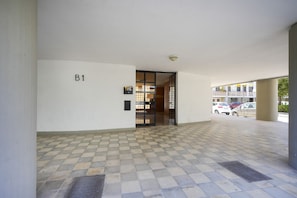 An indoor corridor with a tiled floor, a door labeled 'B1', and a view of parked cars outside.