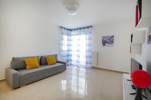 A modern living room with a grey sofa, yellow cushions, a red chair, a flat-screen TV, and a painting on the wall.