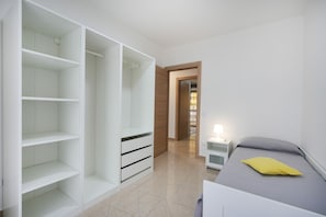 A bedroom with a bed, a nightstand, a white wardrobe, and a door leading to another room.