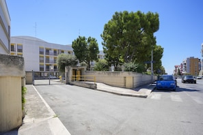 A street view with a building featuring a gated entrance, parked cars, and trees.