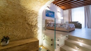 A bedroom with a stone wall, a glass staircase, a bed with a floral bedspread, a sofa, and a painting on the wall.