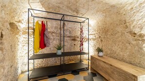 A room with a metal shelving unit displaying clothes, a wooden bench, and a hexagonal tiled floor.