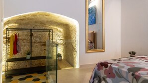 A bedroom with a stone archway, a glass door, a bed with a floral bedspread, a mirror, and a small plant.