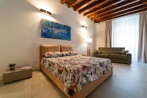 A bedroom with a bed, a sofa, a painting, and a lamp.