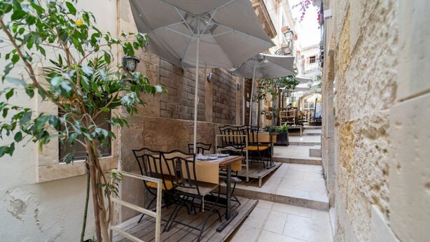 An outdoor café with tables and chairs, a potted plant, and a brick wall.