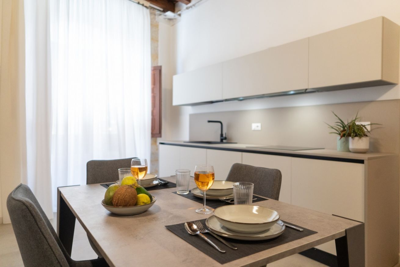 Een moderne eetruimte met een tafel voor twee personen, een schaal fruit en glazen wijn.