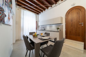 A modern kitchen with a dining area, wooden ceiling beams, and a large wooden door.