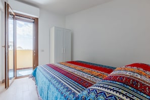 A bedroom with a bed, a wardrobe, and a sliding glass door to a balcony.