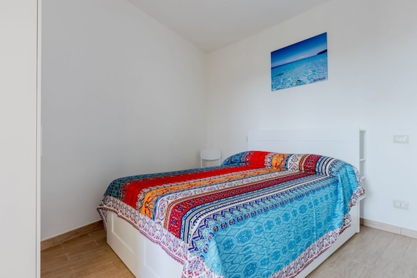 A single-bed room with a colorful bedspread, a white headboard, and a wall-mounted picture.