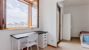 Een slaapkamer met een bed, een bureau met stoel, een raam en een deur.
