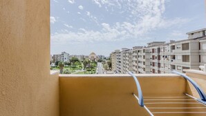 Een balkon met een metalen hekwerk, uitzicht op een woongebied met meerverdiepingen en een heldere lucht.