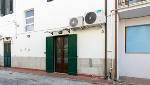 A building with two air conditioning units mounted on the exterior wall, a door with green shutters, and a blue garage door. - GuestHost - Spacious 50 sqm apartment, ideal for 4 people, located on the ground floor of a building WITHOUT lift (NOT suitable for disabled people). The apartment is located a 9-minute walk from Pisa-Galileo Galilei airport and 6 minutes by public trans (Pisa)