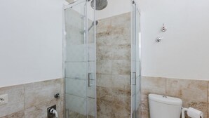 Un baño con cabina de ducha de vidrio, inodoro y pared con azulejos de mármol.