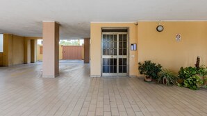 Un espacio exterior cubierto con entrada de puerta de cristal, plantas en macetas y un cartel de prohibido fumar.