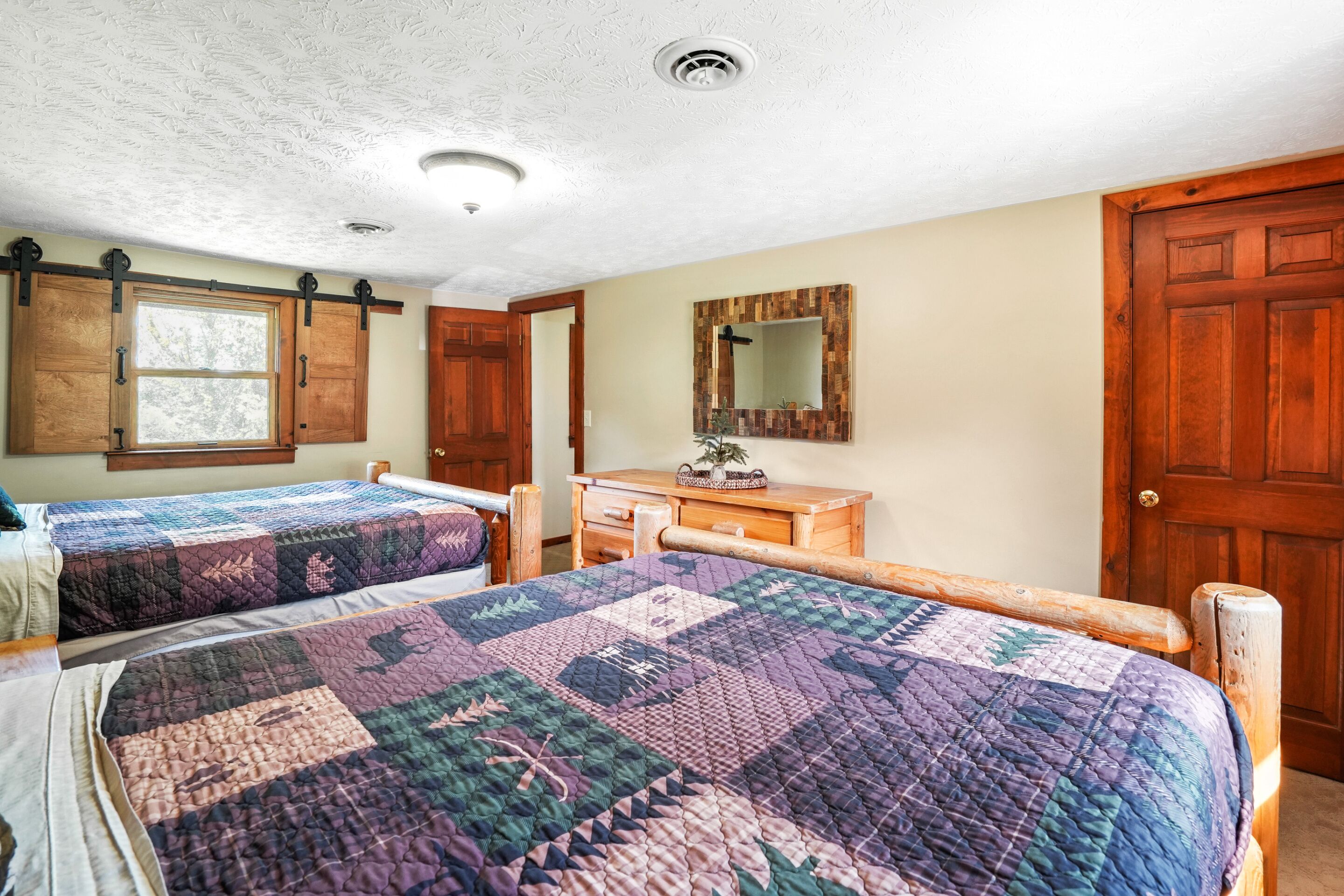 A bedroom with two beds, a dresser, a mirror, and a door.