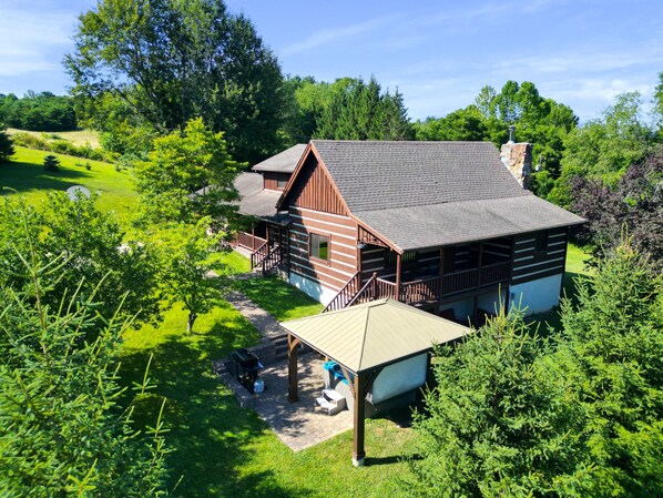 Une cabane en bois dotée d’un porche, entourée d’une végétation luxuriante et d’arbres.