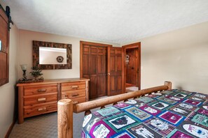Une chambre à coucher avec un lit en bois, une courtepointe aux motifs variés, une commode et une armoire.