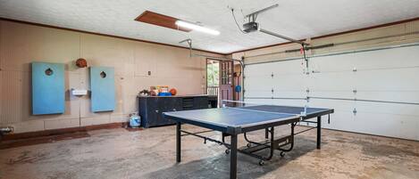 A spacious indoor area with a ping pong table, a ceiling fan, and a garage door.