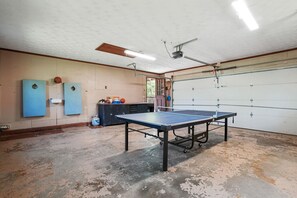 A spacious indoor area with a ping pong table, a ceiling fan, and a garage door.