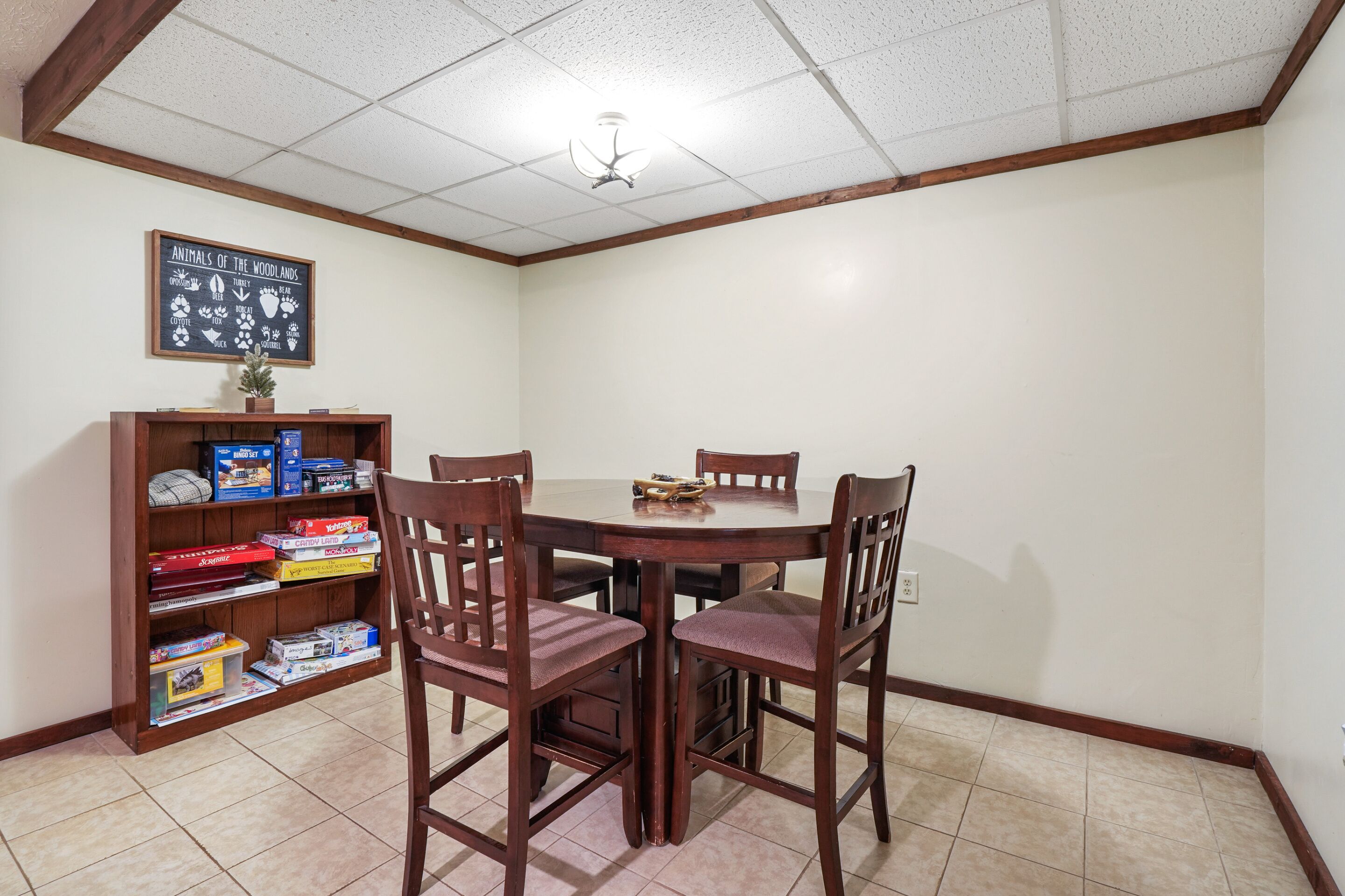 A dining area with a wooden table and chairs, a bookshelf with board games, and a ceiling fan.